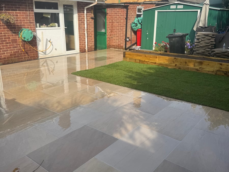 Grey paved patio with lawn and brick pathway.