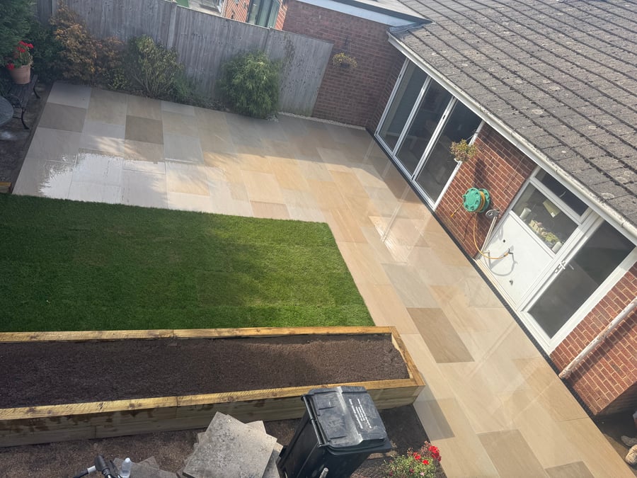 Sandstone patio and pathway wrapping around a lawn and beds.