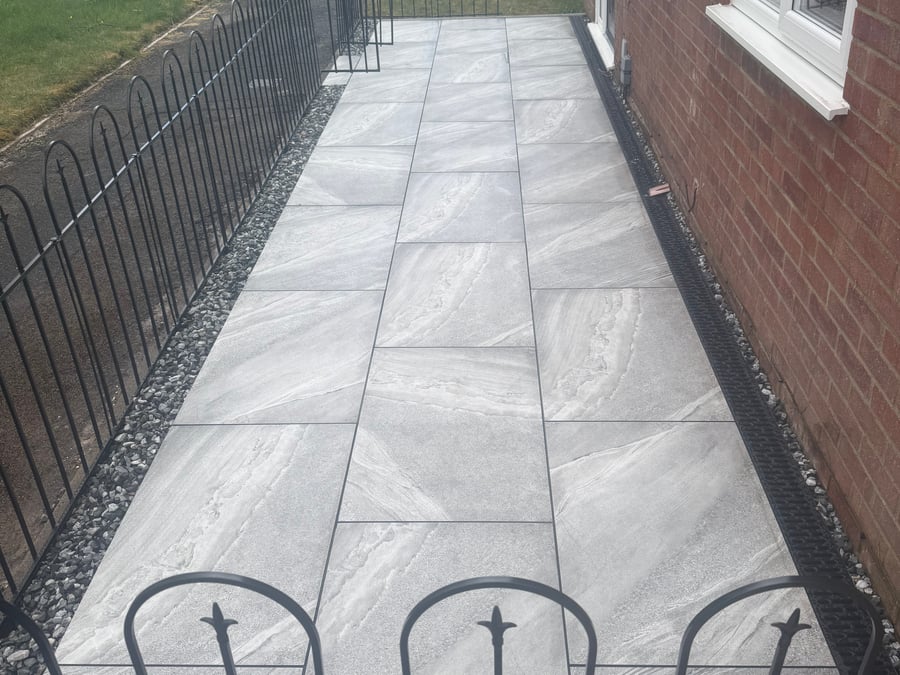 Grey porcelain paving laid alongside the house with pebble trim.
